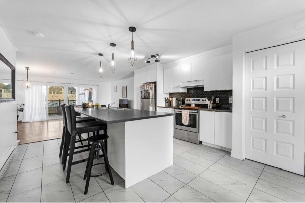 Kitchen with white cabinets, dark grey island with three black stools, and view to living area and balcony. - 22 Rue St-pétersbourg, Gatineau