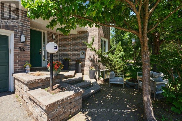 View of townhouse exterior with double garage doors and surrounding trees and grass. - 22 Terrace Drive, Ottawa