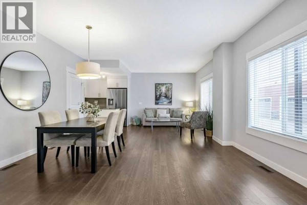 Dining area with a dark wood table, upholstered chairs, and a large window with blinds. - 22 West Coach Manor Sw, Calgary