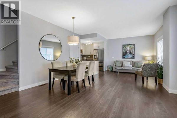 Open-concept living and dining area with a sectional sofa, dining table, and a white kitchen. - 22 West Coach Manor Sw, Calgary
