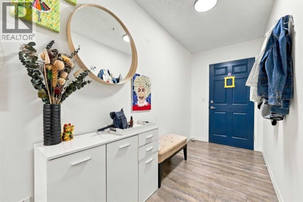 Apartment entryway with a white cabinet, bench, round mirror, and blue door. - 220, 2022 Canyon Meadows Drive Se, Calgary