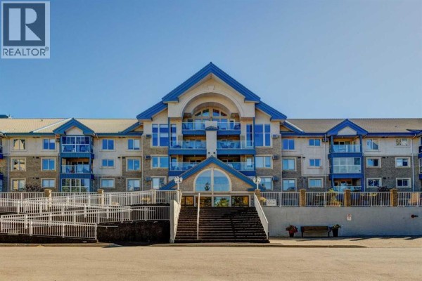 Apartment building exterior with prominent central arch and stairs. - 220, 7229 Sierra Morena Boulevard Sw, Calgary