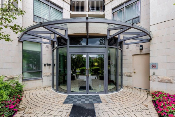 Curved glass and metal entryway with double doors leading into a building. - 220 - 16 Dallimore Circle, Toronto