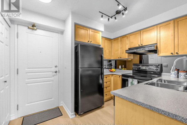 Kitchen with light wood cabinets, black appliances, and a stainless steel sink. - 220 - 16 Dallimore Circle, Toronto
