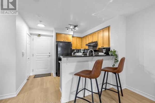 Kitchen with light wood cabinets, a breakfast bar, two stools, and a doorway. - 220 - 16 Dallimore Circle, Toronto