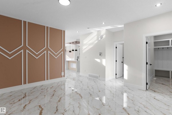 Living room with beige accent wall and bright white marble floors, open to the kitchen area. - 220 21 St Sw, Edmonton