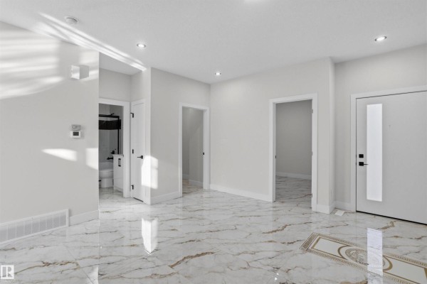 Interior view of a bright foyer with white walls, marble floors, and multiple doorways. - 220 21 St Sw, Edmonton
