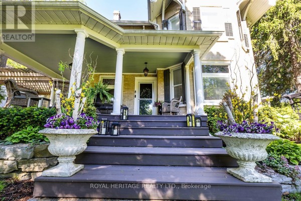 Covered porch with grey wicker furniture, patterned rug, and wooden spool coffee table. - 220 Cochrane Street, Scugog