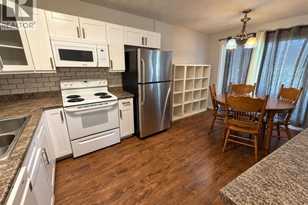 Kitchen and dining area with white cabinets, dining table for four, and sliding glass door. - 220 Mcgill Boulevard W, Lethbridge