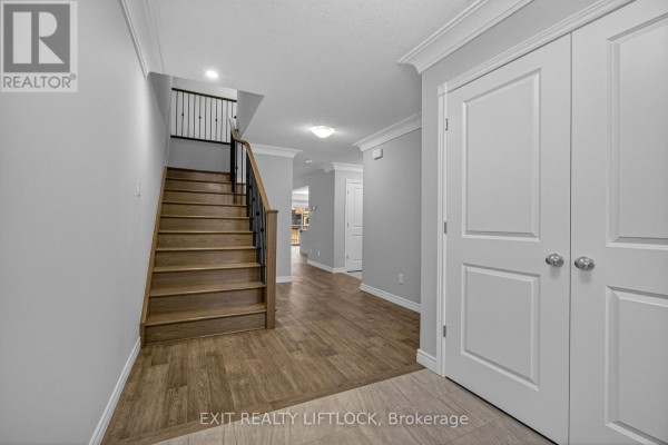 Hallway with a wooden staircase, light gray walls, and double doors. - 220 O'neil Street, Peterborough