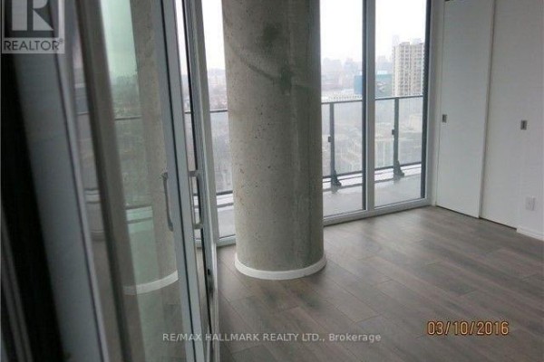 Interior view of a room with a large concrete column, glass doors, and city view. - 2202 - 125 Peter Street, Toronto