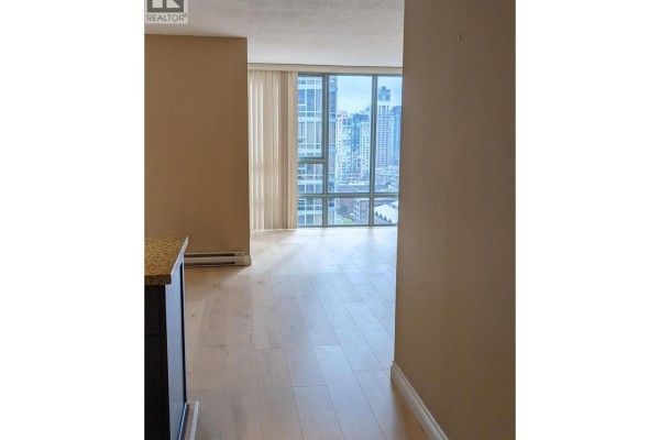 Hallway leading to a living area with light wood floors and a large window with city views. - 2203 930 Cambie Street, Vancouver