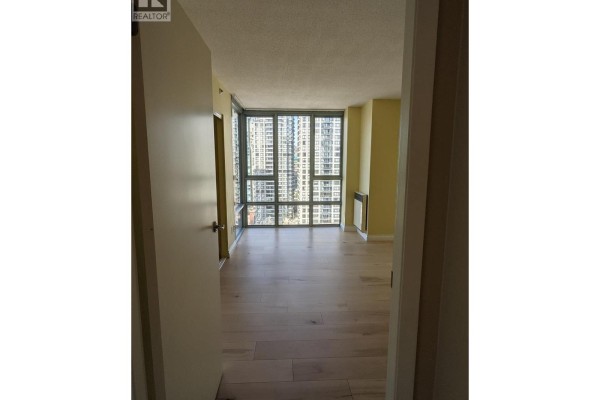 View from an apartment doorway into the living room, showing light wood floors and city skyline. - 2203 930 Cambie Street, Vancouver