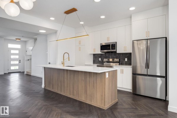 Open concept kitchen and living area with island, stairs, and front door view. - 2203 Crossbill Li Nw, Edmonton