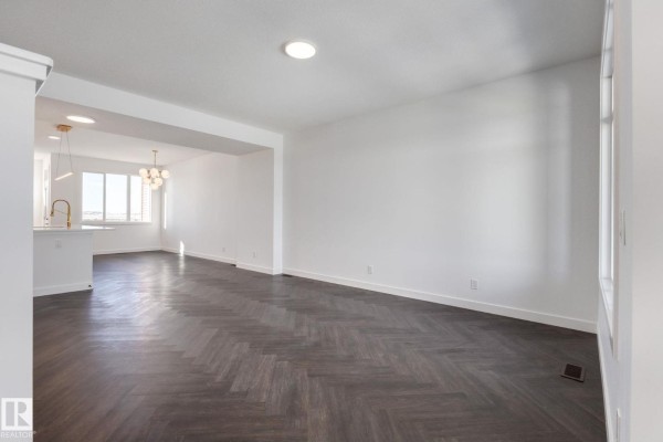 Spacious living room with white walls, dark herringbone flooring, and view of kitchen and dining area. - 2203 Crossbill Li Nw, Edmonton