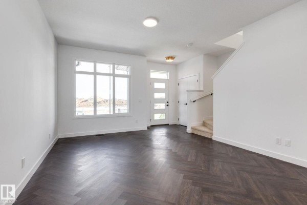 Living room with large windows, front door, and staircase leading upstairs. - 2203 Crossbill Li Nw, Edmonton
