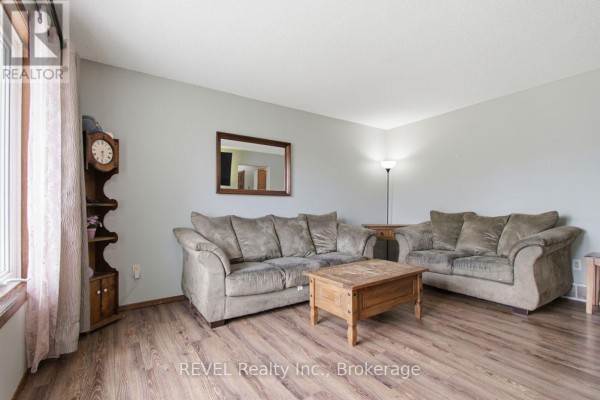 Living room with taupe sofa, armchair, wood coffee table, and wood laminate flooring. - 2203 Stevensville Road, Fort Erie