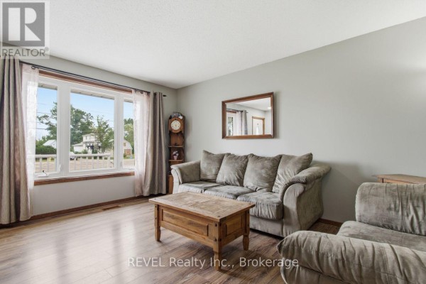 Living room with large window overlooking the street, taupe sofa, and wood laminate flooring. - 2203 Stevensville Road, Fort Erie