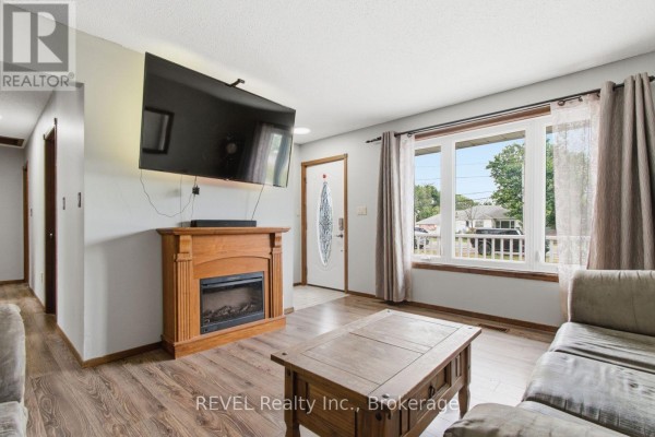 Living room with electric fireplace, mounted television, front door, and wood laminate flooring. - 2203 Stevensville Road, Fort Erie