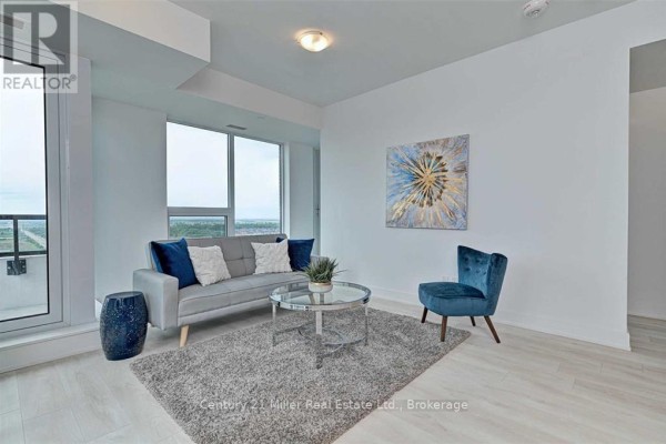 Living room with grey sofa, blue accent chair, textured rug, and large window view. - 2204 - 297 Oak Walk Drive, Oakville