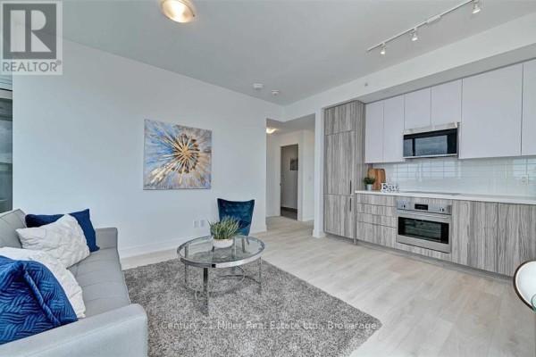 Living space with a sofa, armchair, coffee table, and open concept kitchen with wood cabinets. - 2204 - 297 Oak Walk Drive, Oakville