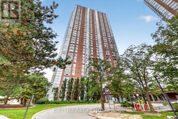 View looking up at a tall brick apartment building with many windows and balconies surrounded by trees. - 2204 - 7 Concorde Place, Toronto