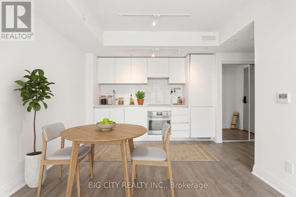 Compact kitchen and dining area with white cabinetry, stainless steel appliances, and a round wooden table. - 2205 - 25 Frederick Todd Way, Toronto