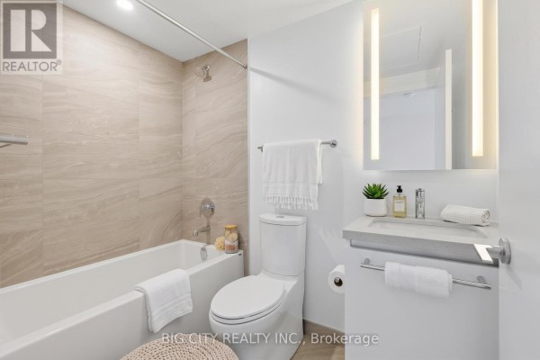 Modern bathroom with a bathtub, toilet, vanity, and tiled walls. - 2205 - 25 Frederick Todd Way, Toronto