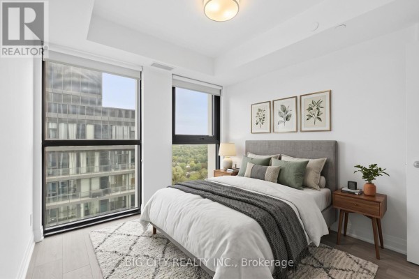 Bedroom with a queen-size bed, nightstand, and large windows overlooking the city skyline. - 2205 - 25 Frederick Todd Way, Toronto