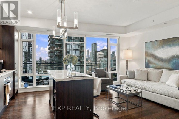 Living room with a grey sofa, armchair, coffee table, and panoramic city view. - 2206 - 21 Widmer Street, Toronto