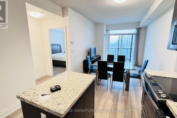 View of a dining table with black chairs next to a living room area and an open doorway to a bedroom. - 2206 - 3600 Hwy 7, Vaughan
