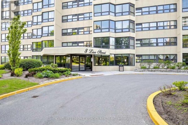 Entrance to the apartment building at 8 Lisa Street with a covered walkway, landscaping, and asphalt driveway. - 2207 - 8 Lisa Street, Brampton