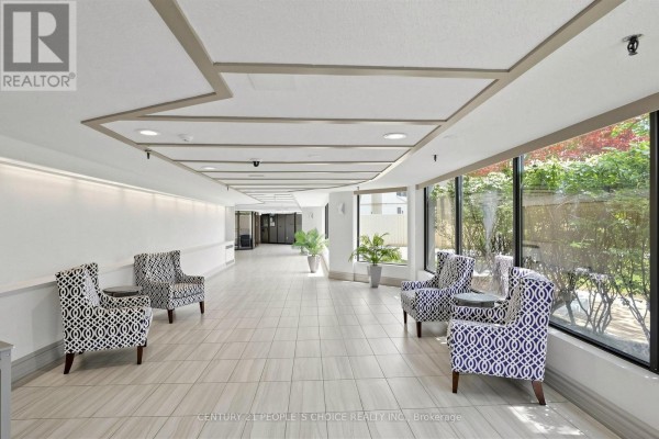 Building lobby with light tile floors, geometric patterned armchairs, and large windows looking out to greenery. - 2207 - 8 Lisa Street, Brampton