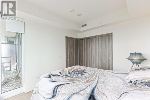 Bedroom with a bed, balcony door with glass railing, and grey sliding closet doors. - 2207 - 95 Mcmahon Drive, Toronto