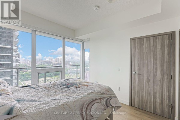 Bedroom with a bed, floor-to-ceiling windows with city views, and a grey wooden door. - 2207 - 95 Mcmahon Drive, Toronto