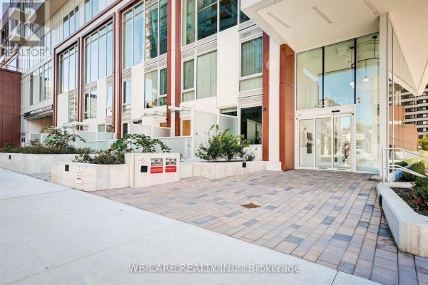 Building entrance with automatic glass doors and an outdoor seating area with modern planters. - 2208 - 33 Helendale Avenue, Toronto