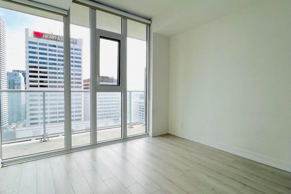 Empty room with light wood laminate flooring and floor-to-ceiling windows offering panoramic city views. - 2208 - 33 Helendale Avenue, Toronto
