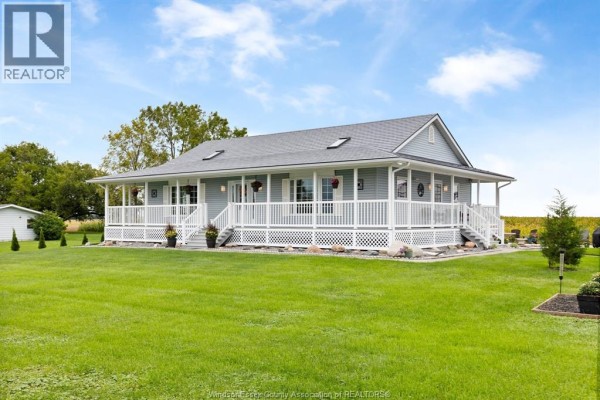 Light blue house with a white wrap-around porch, white railings, and stairs, set on a green lawn. - 2208 County Rd 20 West, Essex
