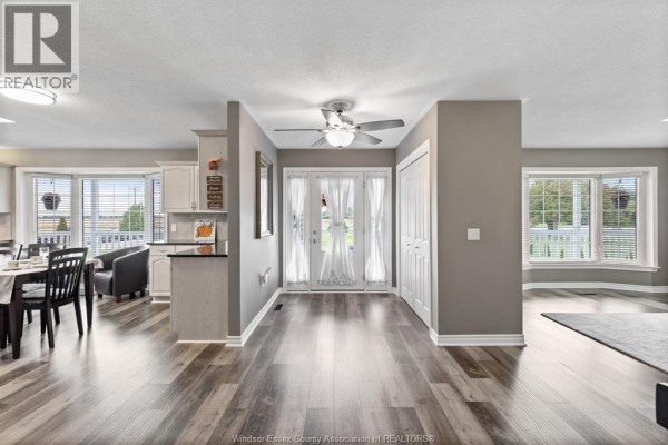 Interior view of a hallway with double glass doors, grey walls, and dark wood plank flooring leading to a dining area and living room. - 2208 County Rd 20 West, Essex