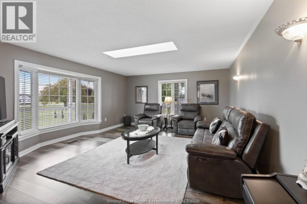 Living room with dark brown leather couches, a grey rug, bay windows, and grey walls, featuring a ceiling fan and wall sconces. - 2208 County Rd 20 West, Essex