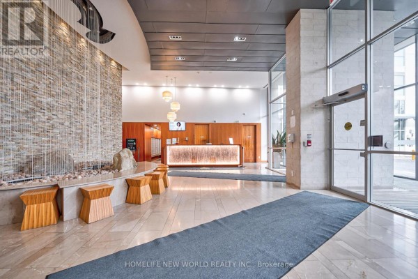 Building lobby featuring a stone water feature, wooden reception desk, and marble floors. - 2209 - 225 Webb Drive, Mississauga
