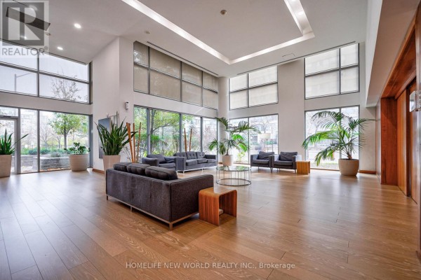 Spacious building lounge area with sofas, glass coffee tables, and large windows overlooking greenery. - 2209 - 225 Webb Drive, Mississauga