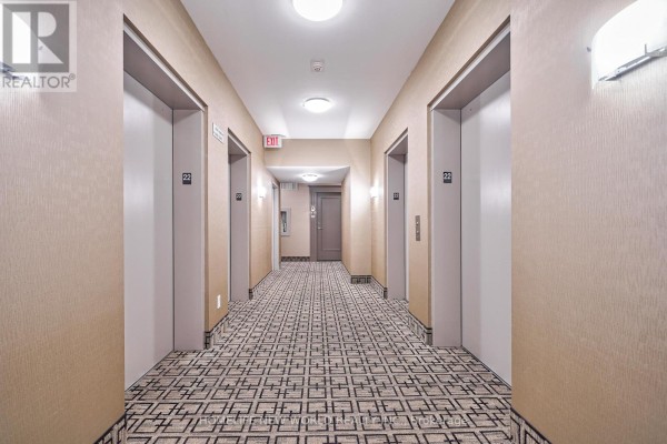 Hallway with patterned carpet, two elevators, and doors leading to apartments. - 2209 - 225 Webb Drive, Mississauga