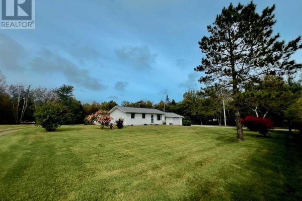 Wide exterior view of the white bungalow and surrounding green lawn with trees. - 2209 Lingan Road Road, Lingan