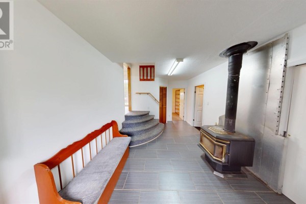 Interior view of a hallway with a wood stove, bench, and curved stairs. - 2209 Lingan Road Road, Lingan