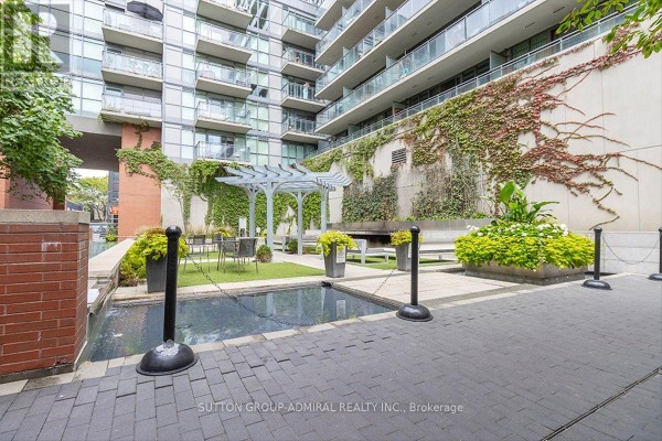 Outdoor courtyard with a water feature, seating area under a pergola, and lush landscaping. - 221 - 775 King Street W, Toronto