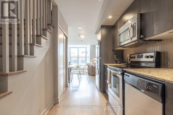 Modern kitchen with stainless steel appliances, granite countertops, and adjacent staircase leading upstairs. - 221 - 775 King Street W, Toronto