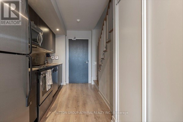Kitchen area with stainless steel appliances and wood-look flooring, next to a closet and staircase. - 221 - 775 King Street W, Toronto
