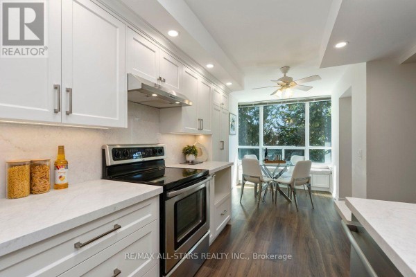 Kitchen with stainless steel stove, white cabinets, quartz counters, and dining area. - 221 - 85 The Boardwalk Way, Markham