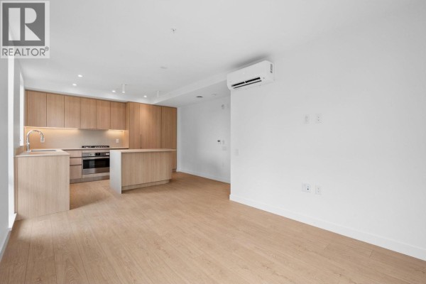 Empty living space with a kitchen area, featuring light wood cabinets and light wood floors. - 221 2820 Nanaimo Street, Vancouver